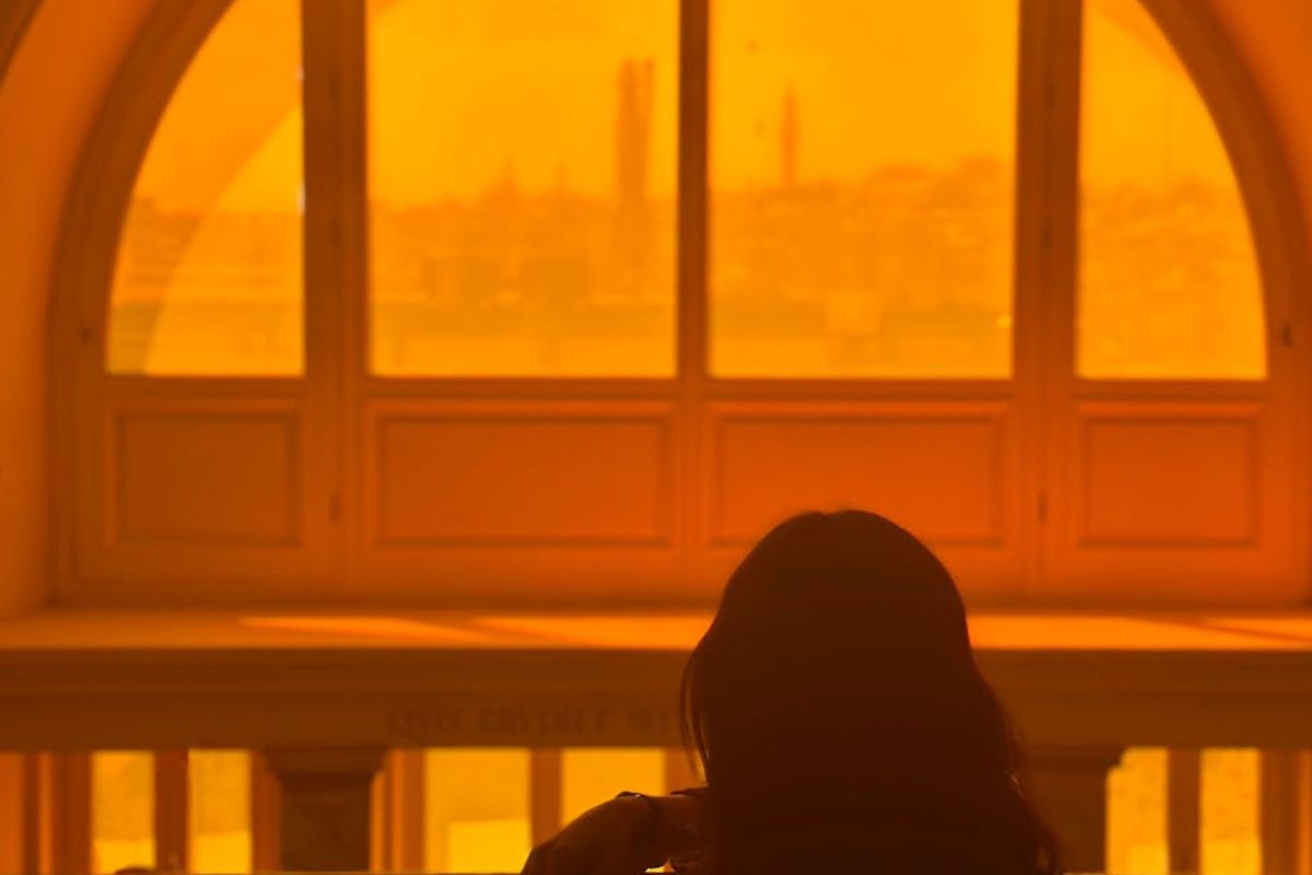 Person meditatively looking out a large window at nature